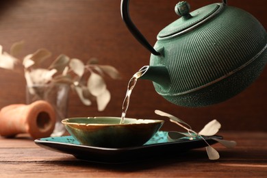 Photo of Pouring freshly brewed tea from teapot into cup on wooden table. Traditional ceremony