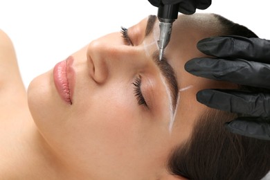 Beautician making permanent eyebrow makeup to young woman on white background, closeup