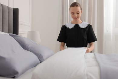 Photo of Young maid making bed in hotel room