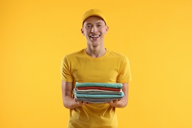 Photo of Dry-cleaning delivery. Happy courier holding folded clothes on orange background