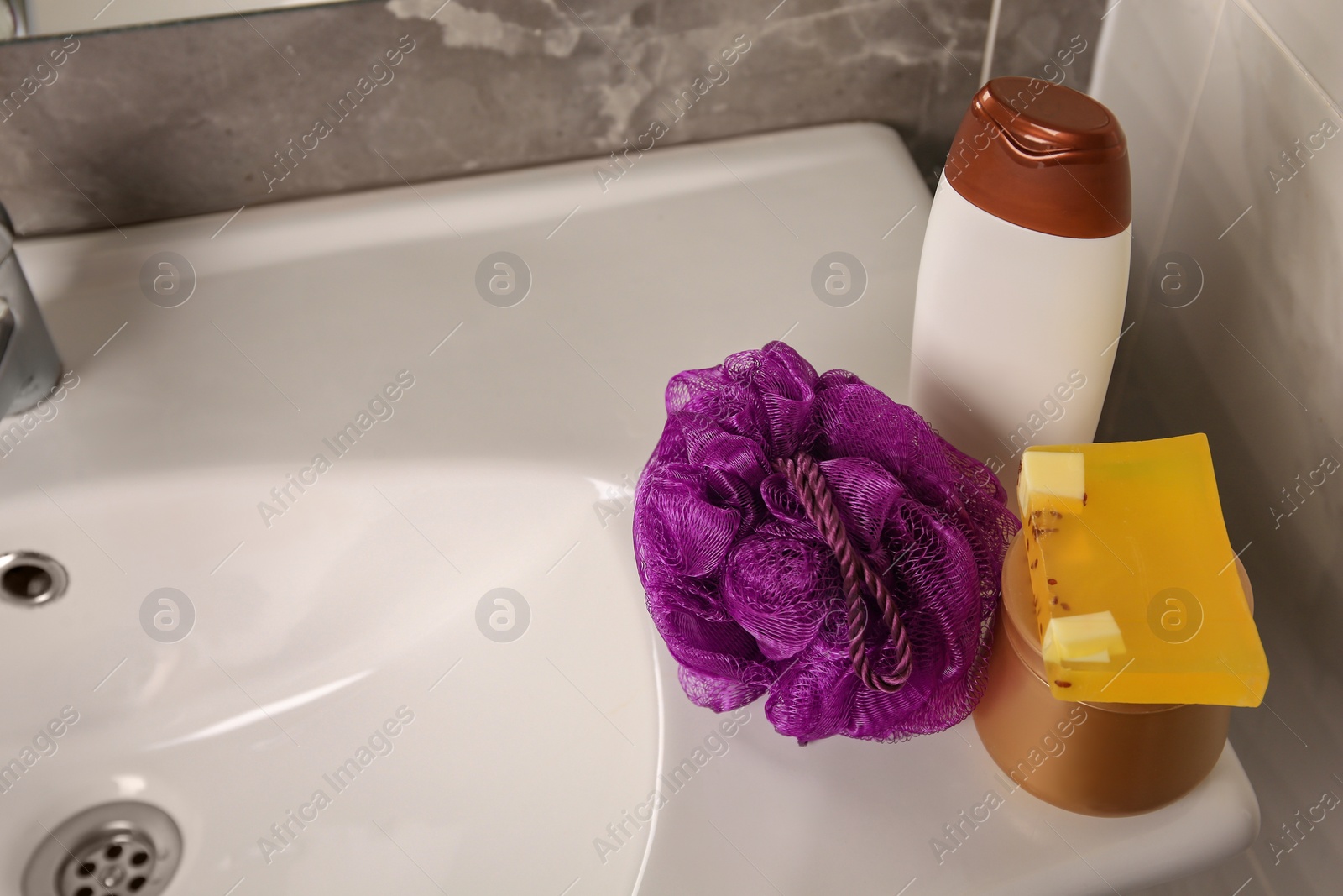 Photo of Purple shower puff and cosmetic products on sink in bathroom, space for text