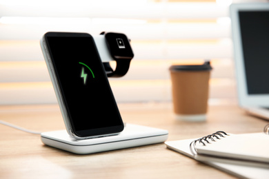 Photo of Mobile phone and smartwatch with wireless charger on wooden table. Modern workplace accessory