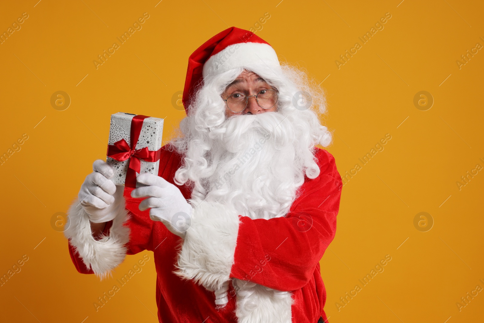 Photo of Santa Claus holding Christmas gift on orange background