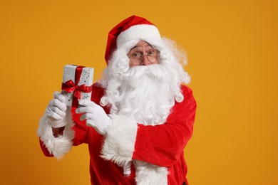 Photo of Santa Claus holding Christmas gift on orange background