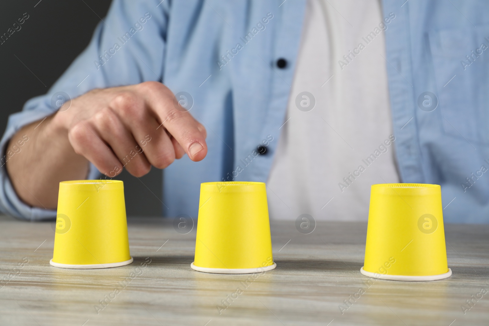 Photo of Man playing shell game at wooden table, closeup