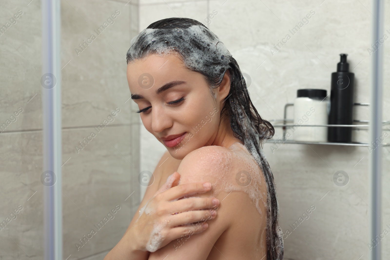 Photo of Beautiful woman washing hair with shampoo in shower