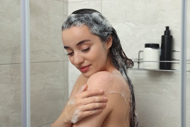 Photo of Beautiful woman washing hair with shampoo in shower