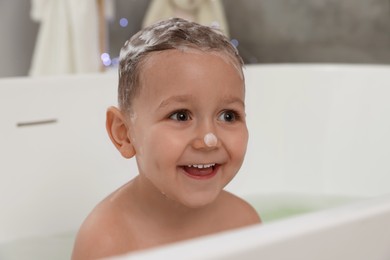 Photo of Cute little boy washing hair with shampoo in bathroom