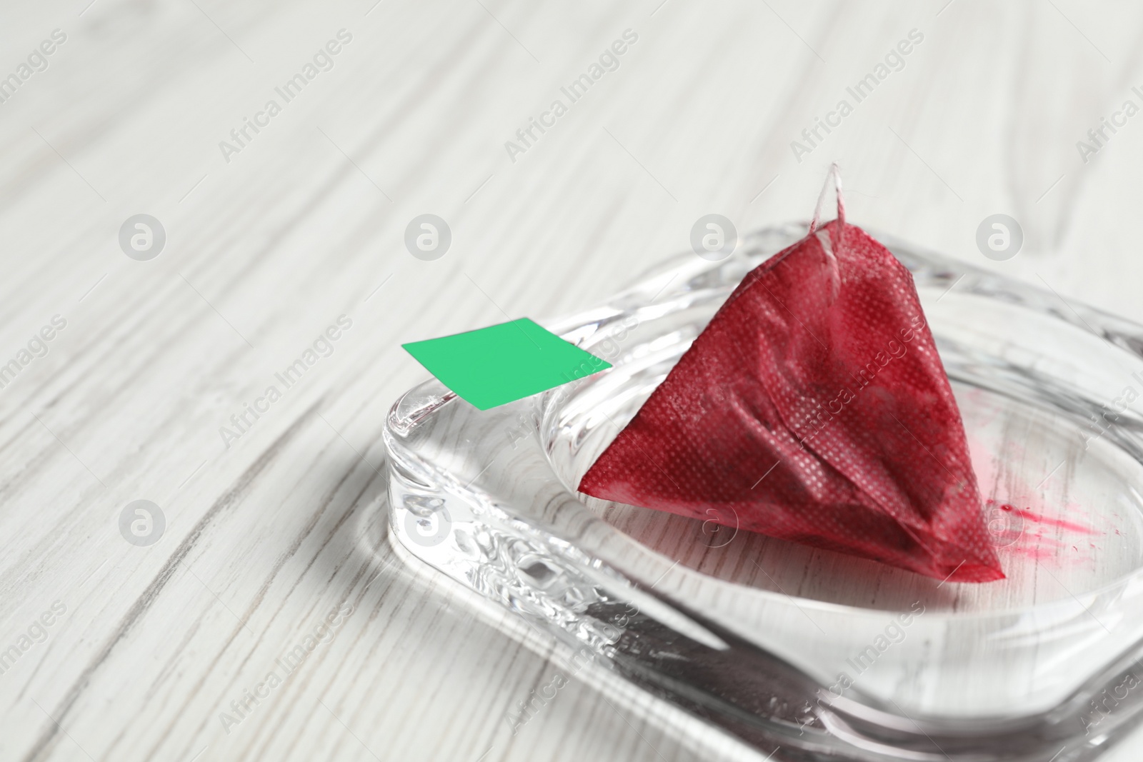 Photo of Saucer with used pyramid tea bag on white wooden table, closeup. Space for text