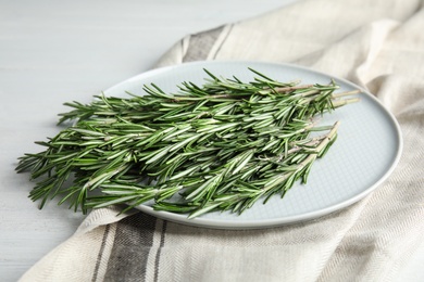 Photo of Plate with fresh rosemary twigs on wooden table