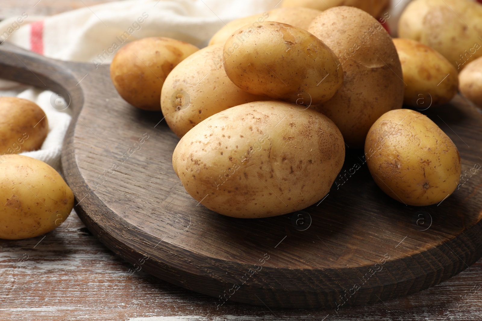 Photo of Raw fresh potatoes and cutting board on wooden table, closeup