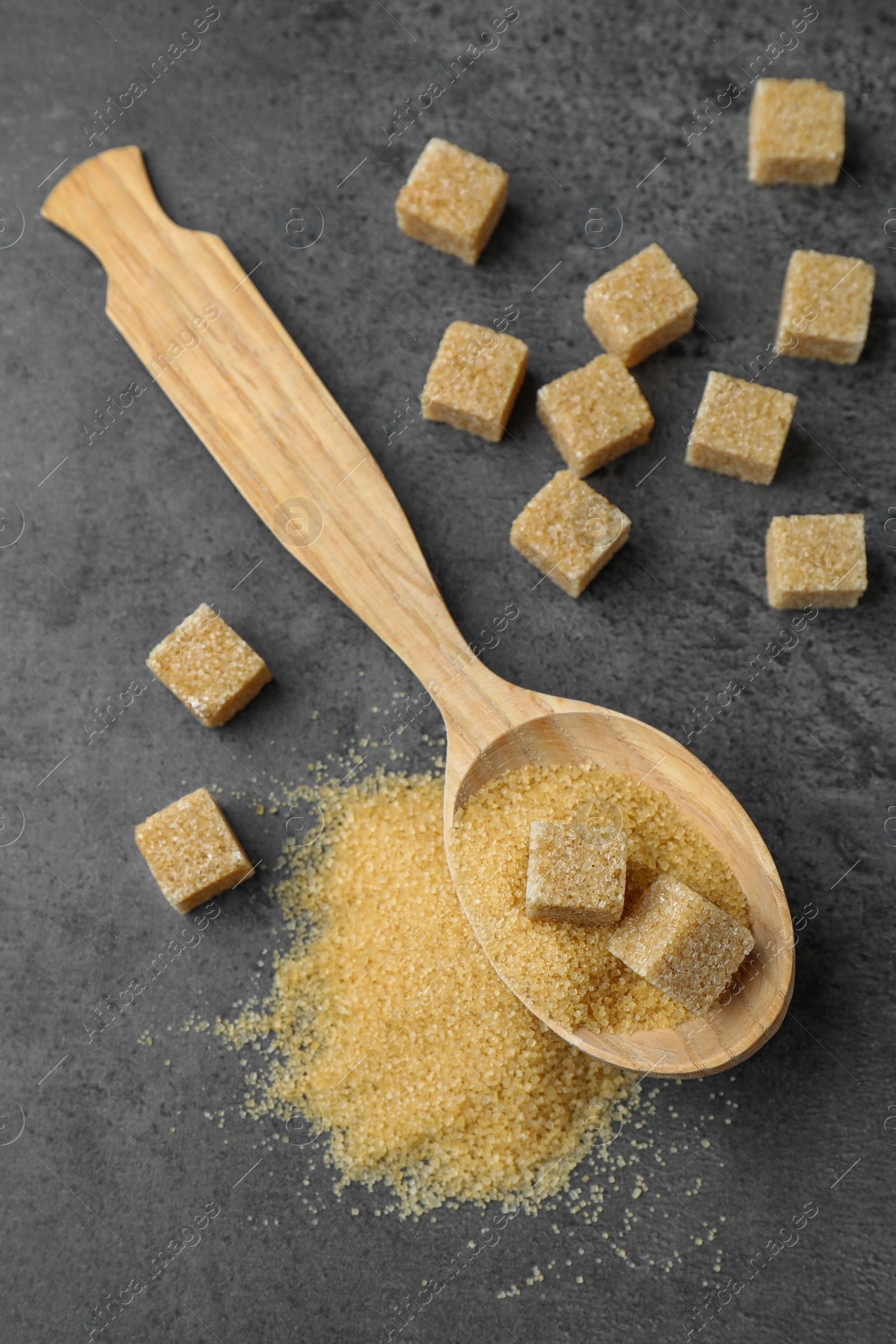 Photo of Spoon with brown sugar cubes on grey table, flat lay