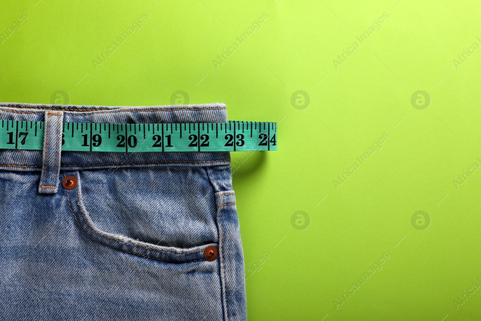 Photo of Jeans and measuring tape on light green background, top view with space for text. Weight loss concept