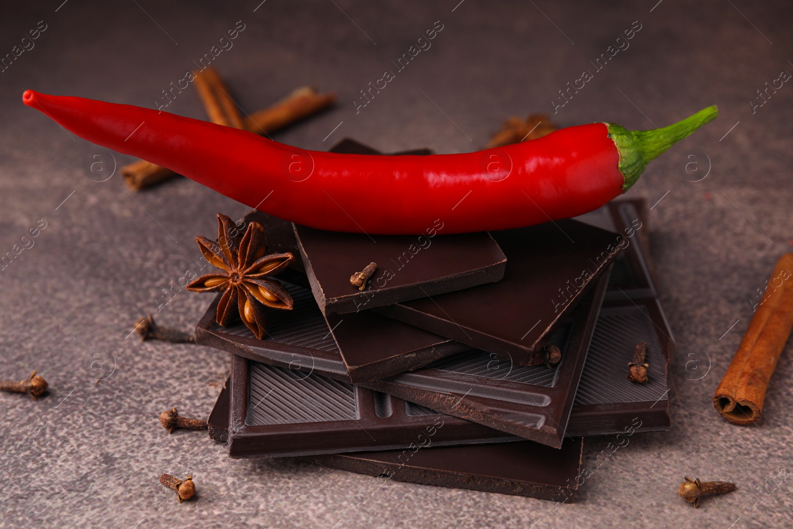 Photo of Delicious chocolate, fresh red chili pepper and spices on grey textured table