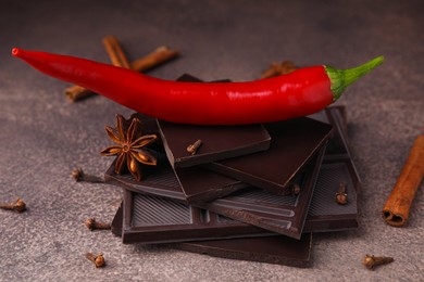 Photo of Delicious chocolate, fresh red chili pepper and spices on grey textured table
