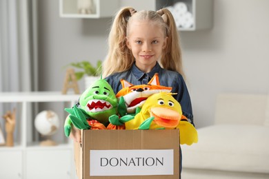 Cute little girl holding donation box with soft toys at home