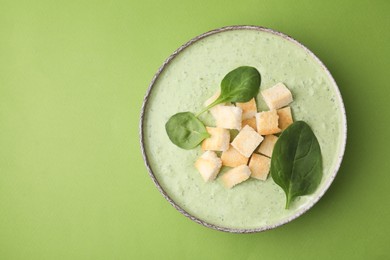 Photo of Delicious spinach cream soup with leaves and croutons in bowl on green background, top view