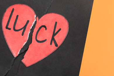 Photo of Torn heart and word LUCK written in notebook on orange background, above view