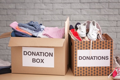 Donation boxes with clothes and shoes on table against brick wall