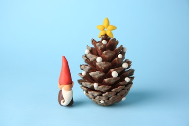 Photo of Beautiful plasticine dwarf with pinecone on light blue background. Children's handmade ideas