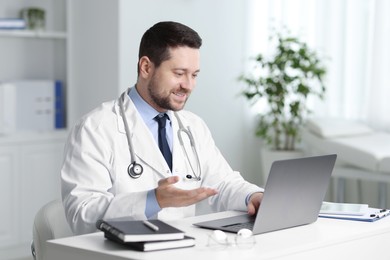 Photo of Smiling doctor having online consultation via laptop at table in clinic