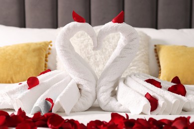 Photo of Honeymoon. Swans made with towels and beautiful rose petals on bed, closeup