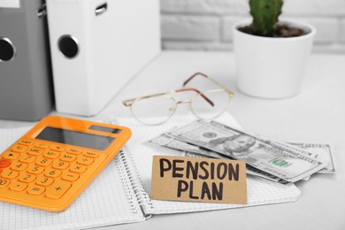 Photo of Card with phrase Pension Plan, dollar banknotes, calculator and notebook on white office table