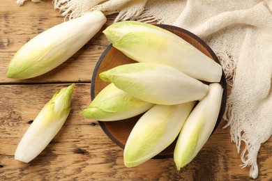 Photo of Fresh raw Belgian endives (chicory) and bowl on wooden table, top view