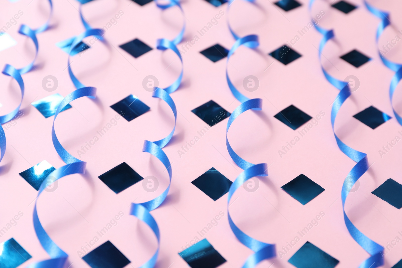 Photo of Shiny blue serpentine streamers and confetti on pink background, closeup