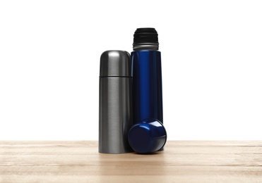 Photo of Stylish thermo bottles on wooden table against white background