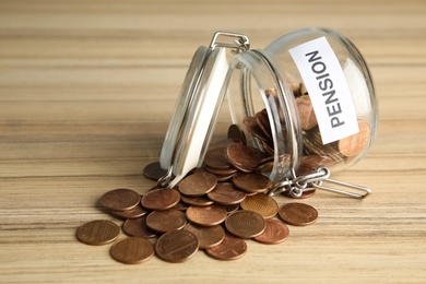 Photo of Glass jar with label PENSION and coins on wooden table
