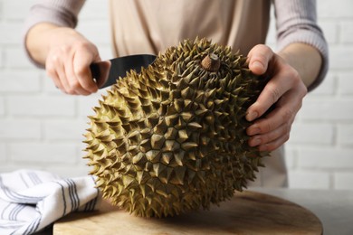 Photo of Woman cutting fresh ripe durian at table, closeup