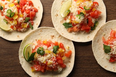 Photo of Delicious tacos with vegetables and lime on wooden table, top view