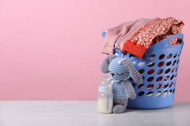 Photo of Laundry basket with baby clothes near crochet toy and bottle on white marble table, space for text
