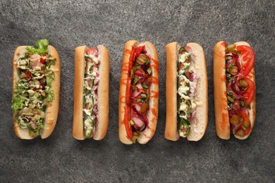 Photo of Delicious hot dogs with different toppings on grey table, flat lay