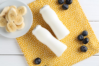 Photo of Tasty yogurt in bottles, banana and blueberries on white wooden table, top view