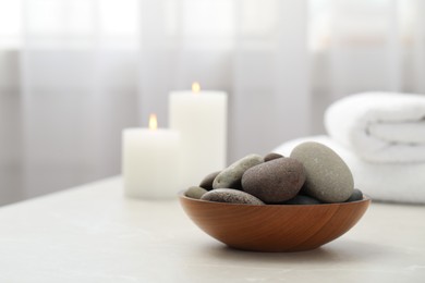 Photo of Spa stones in wooden bowl on white table indoors. Space for text