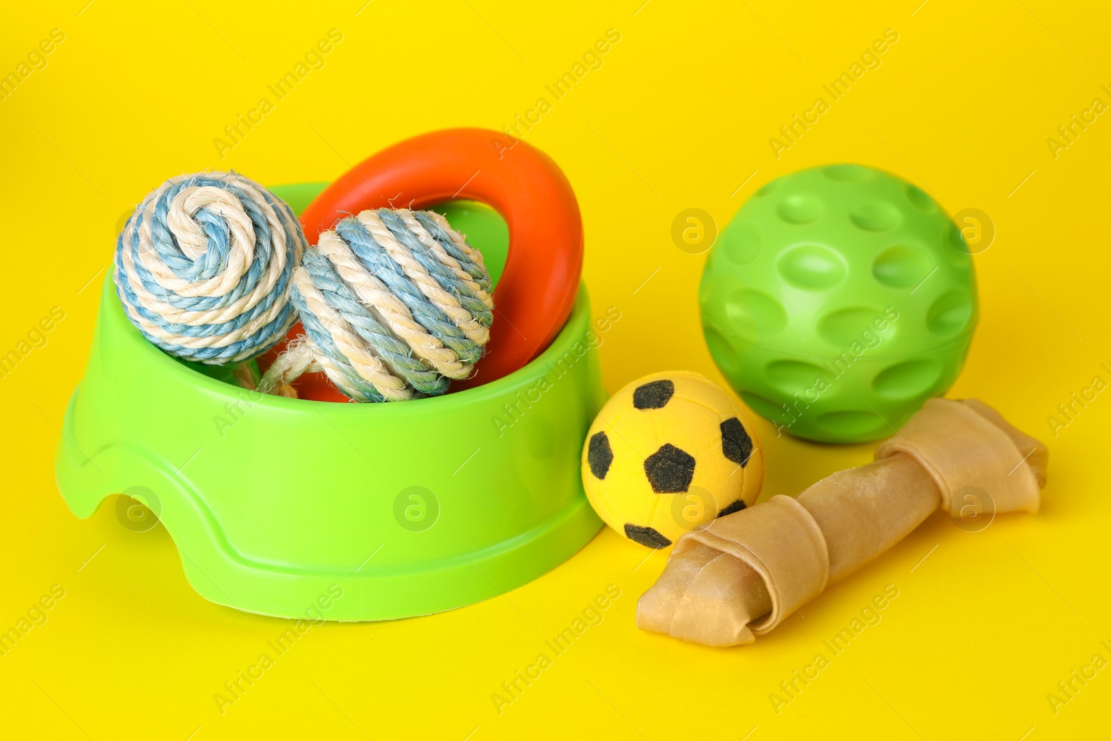 Photo of Various bright pet toys and bowl on yellow background