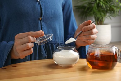 Photo of Woman adding sugar into aromatic tea at wooden table indoors, closeup
