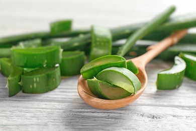Photo of Spoon with slices of aloe vera on wooden table, closeup