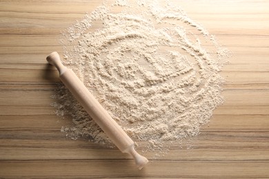 Photo of Scattered flour and rolling pin on wooden table, top view