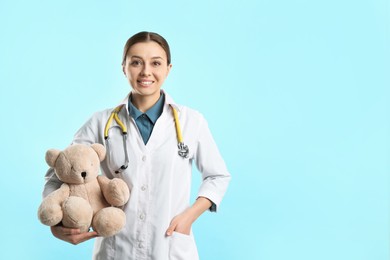 Photo of Pediatrician with teddy bear and stethoscope on turquoise background, space for text