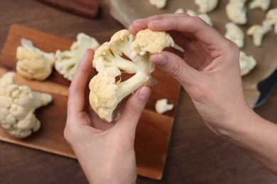 Photo of Woman holding fresh cauliflower at wooden table, above view