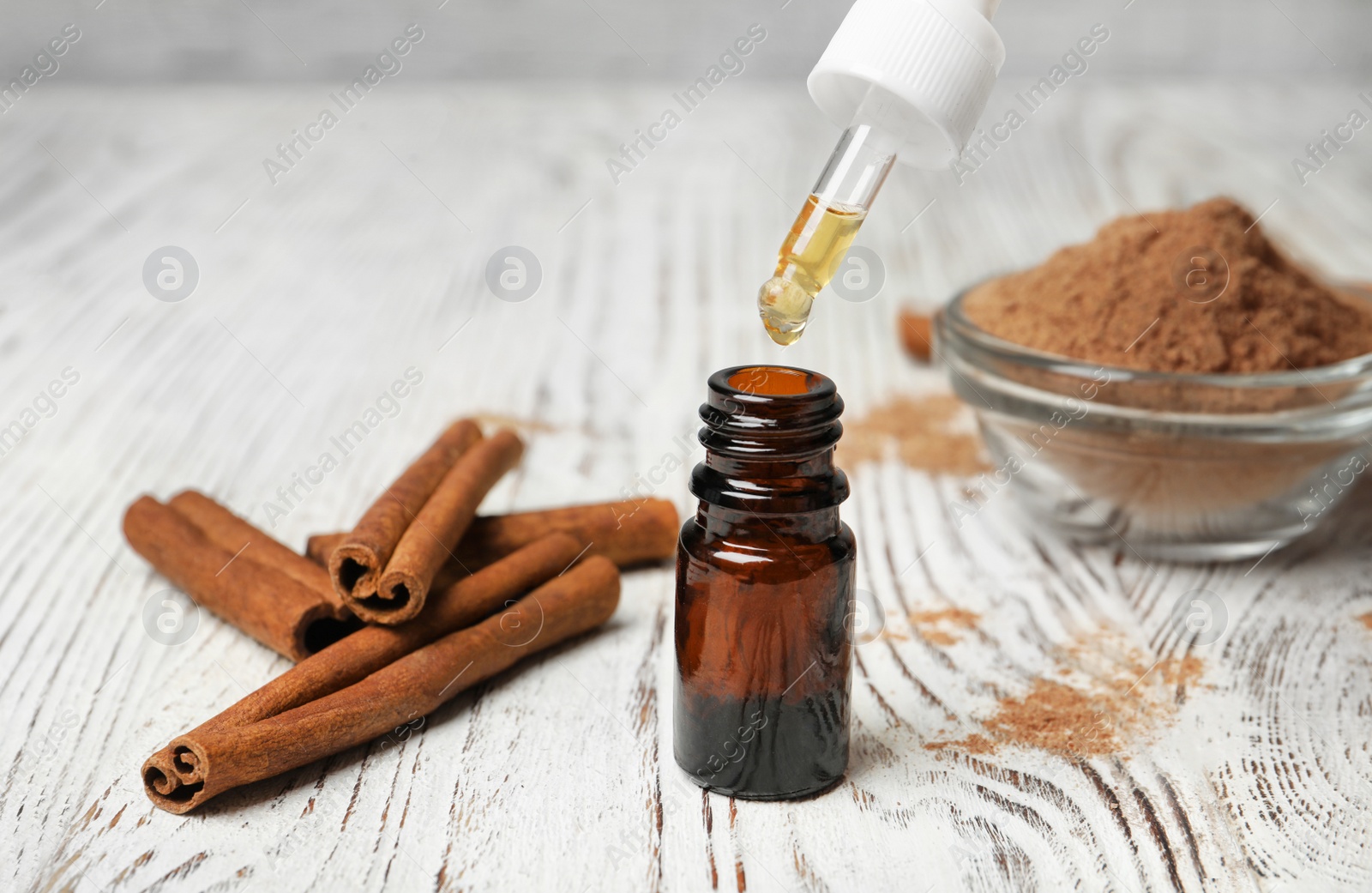 Photo of Bottle with cinnamon oil, powder and sticks on wooden table