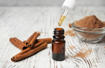 Photo of Bottle with cinnamon oil, powder and sticks on wooden table