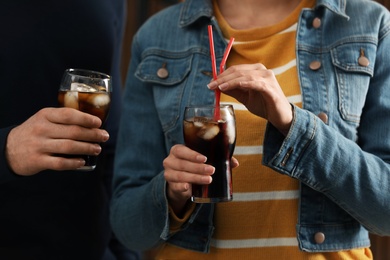 Photo of People holding glasses of cola with ice on blurred background, closeup