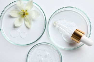 Photo of Petri dishes with samples of cosmetic oil, pipette and beautiful flower on white background, flat lay