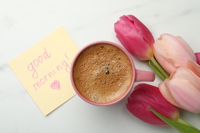 Photo of Cup of aromatic coffee, beautiful pink tulips and Good Morning note on white marble table, flat lay