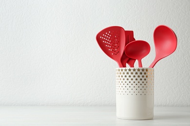 Set of kitchen utensils in stand on wooden table near light wall. Space for text