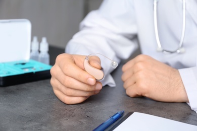 Photo of Doctor holding hearing aid at table, closeup. Medical objects